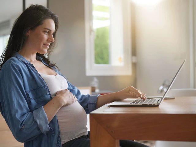 Pregnant woman sitting at a desk, gently holding her belly with one hand while using a laptop with the other.