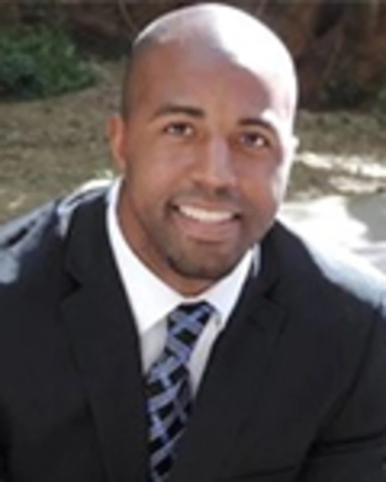 Person wearing a dark suit, white shirt, and patterned tie smiling outdoors.