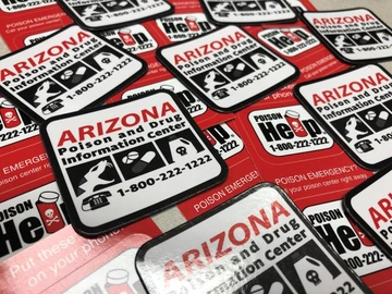 Pile of Arizona Poison and Drug Information Center magnets and stickers showing the logo and 1-800-222-1222 hotline.