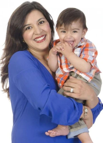Smiling woman in a blue blouse holding a laughing baby wearing an orange plaid shirt.